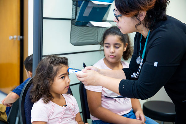 a child gets her temperate checked on her forehead by a MAP clinic employee
