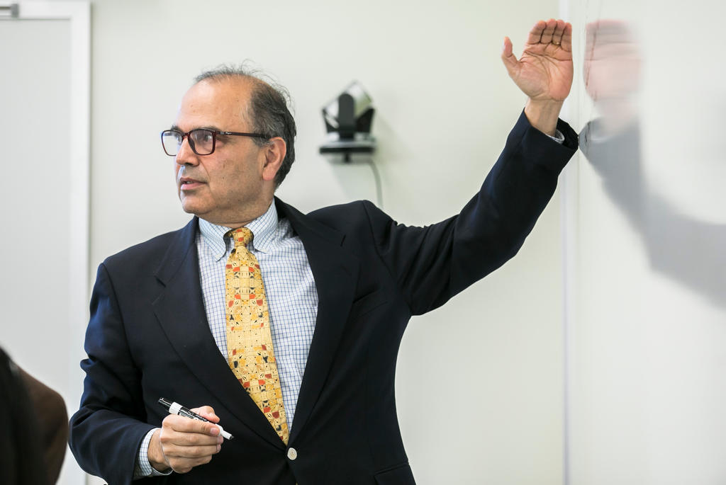 Dr. Farrokh Alemi teaching a class gesturing to whiteboard with marker in hand